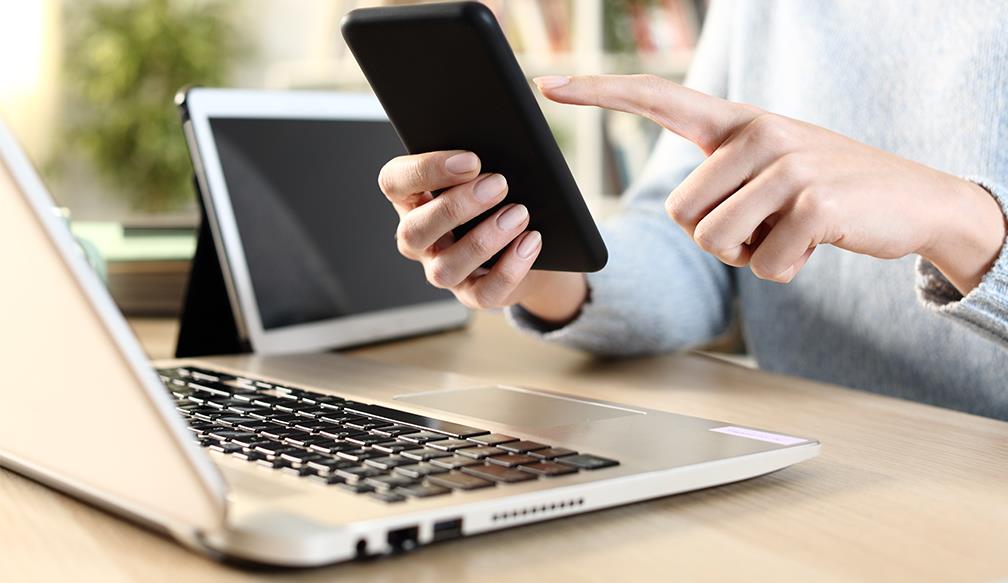 Someone using a phone next to a laptop and a tablet