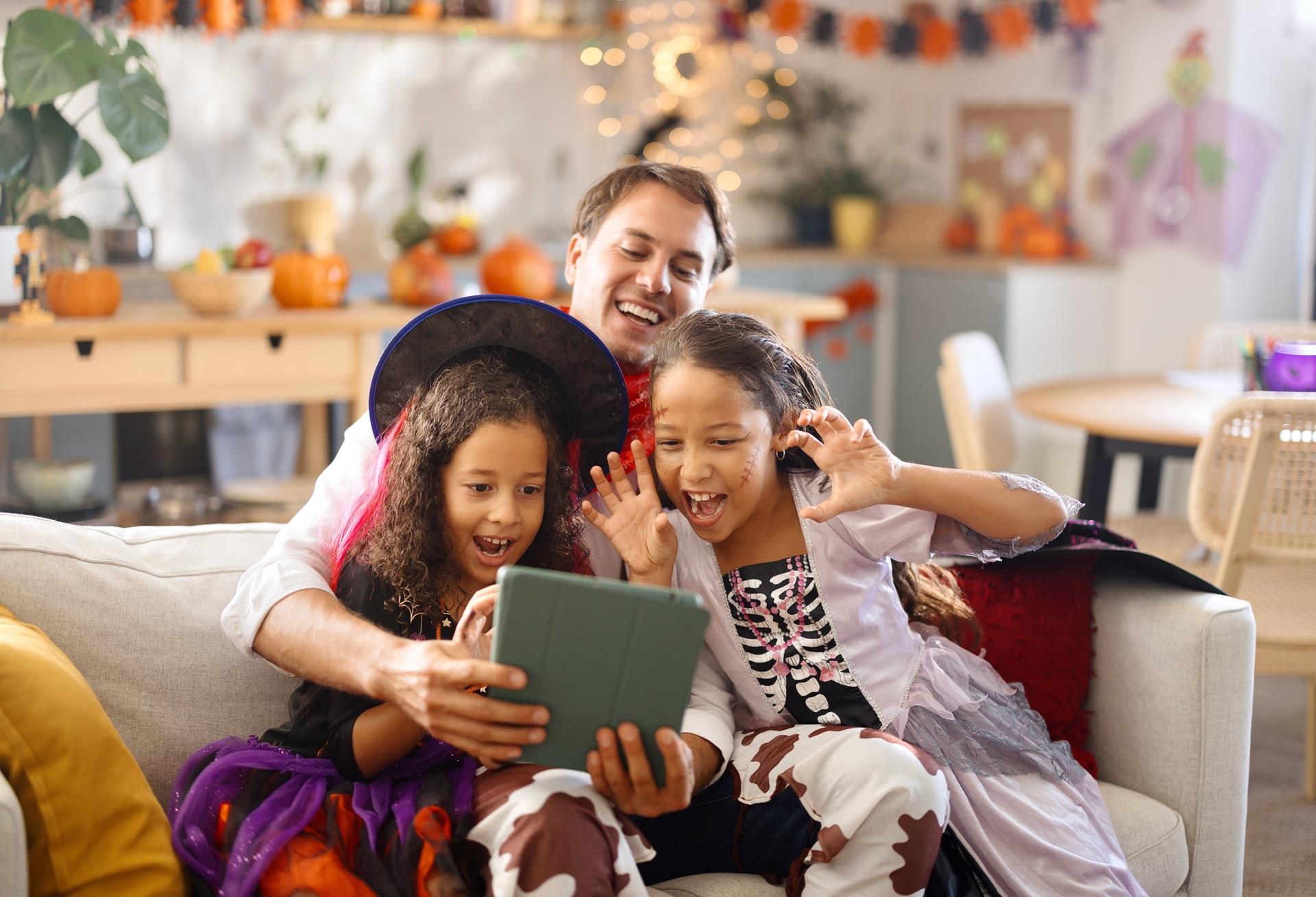Dad and two kids in Halloween costumes streaming on a tablet with strong home Wi-Fi